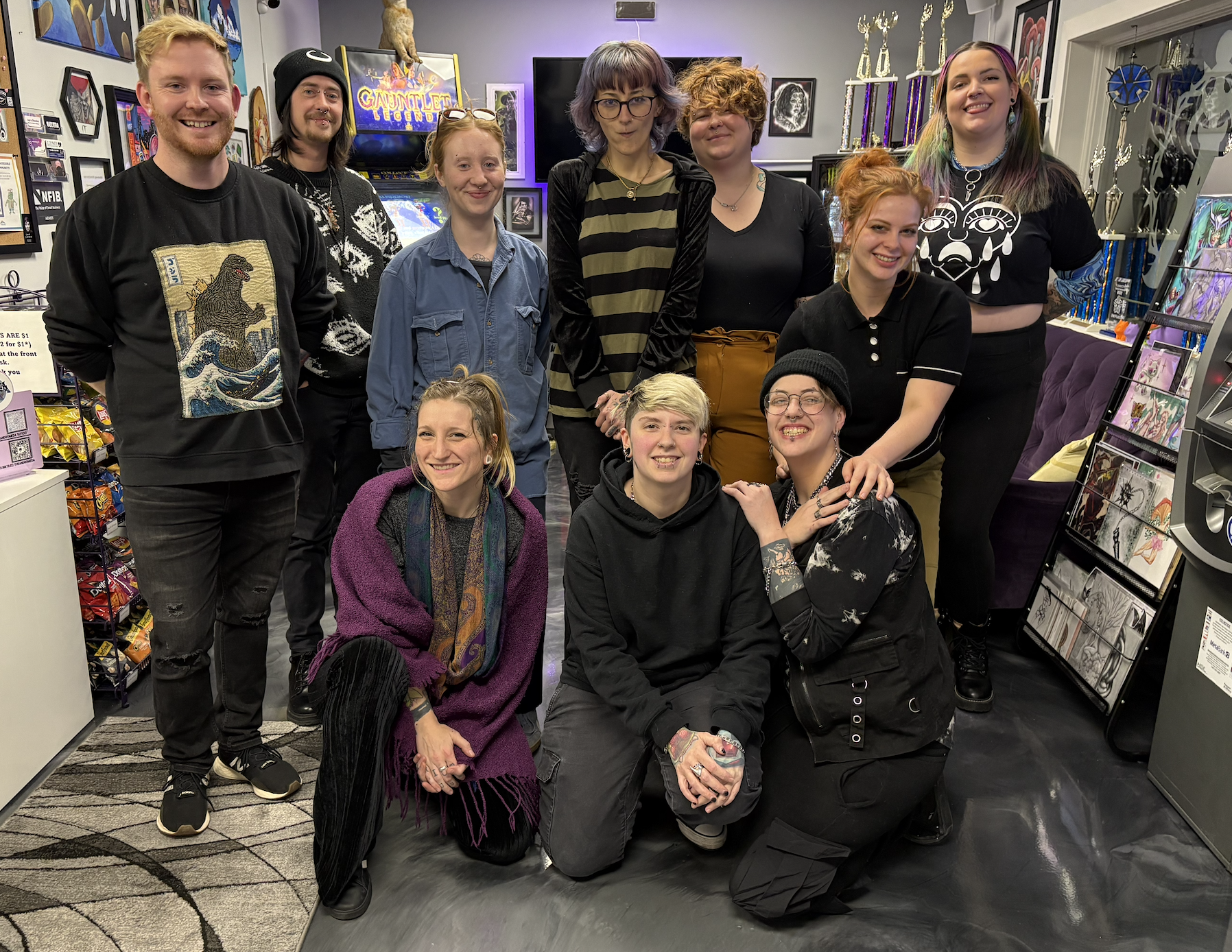 Group of ten people gathering in a decorated room, some posing and smiling, with prizes and artwork displayed around them.