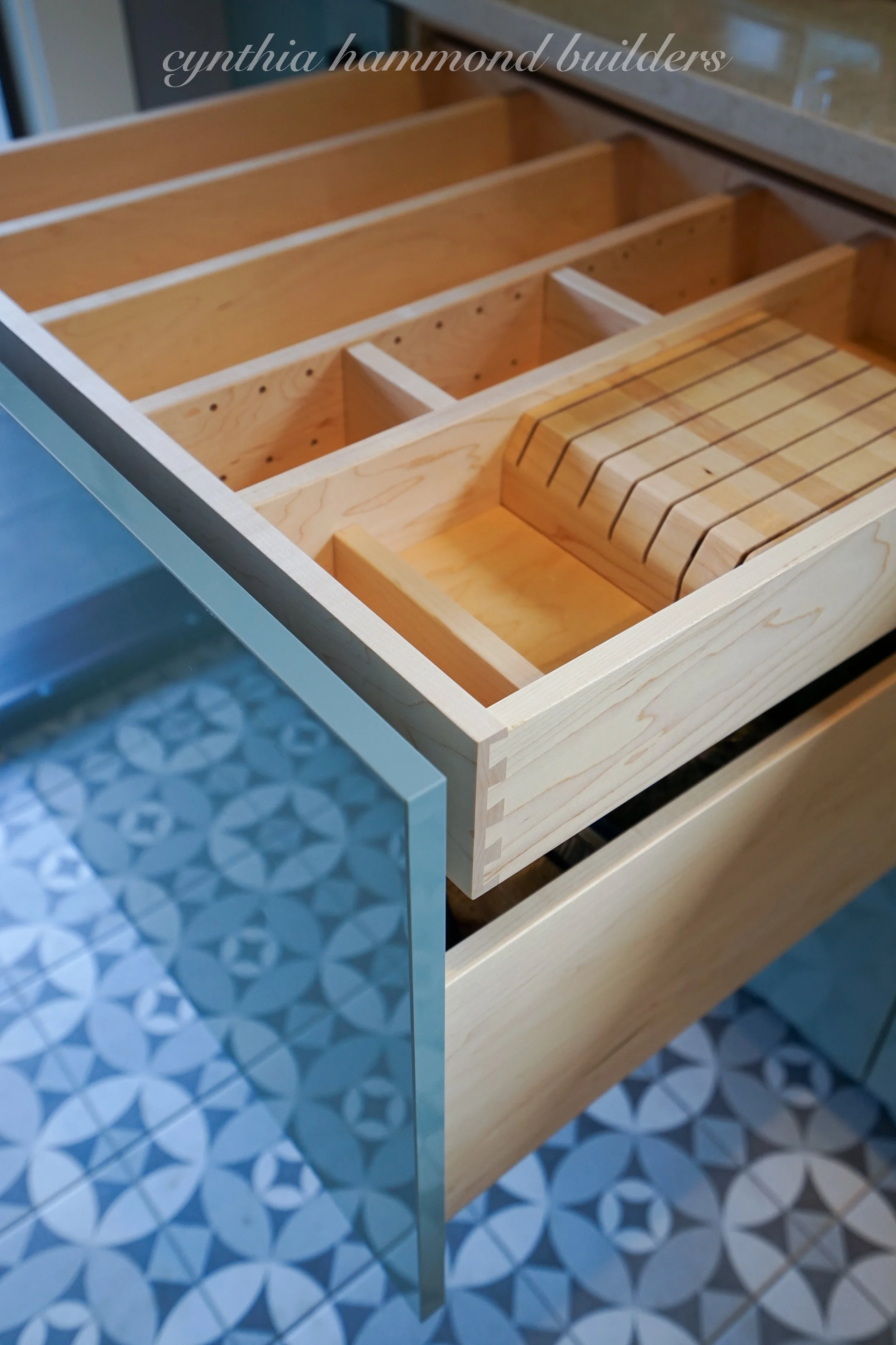 Custom wood drawer organizer pulled open above blue patterned floor tile