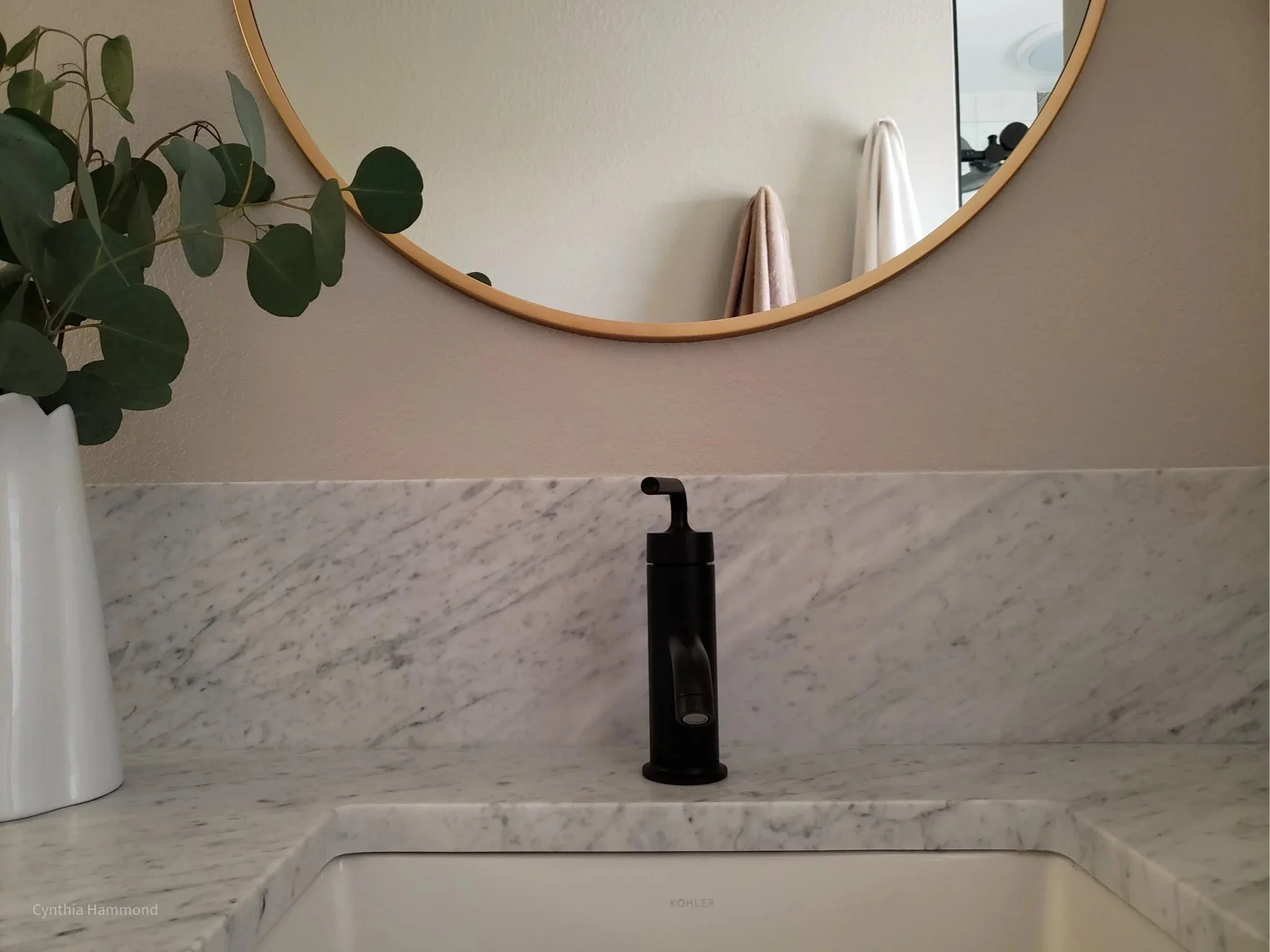 Bathroom sink with a black faucet, marble backsplash, and round mirror