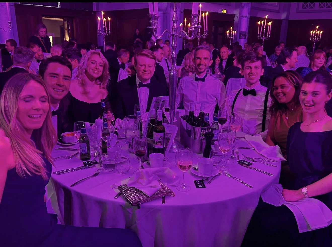 A modern building with a section of wooden vertical slats and large glass window, situated in a mountainous landscape with dry grass and sparse trees, under an overcast sky.