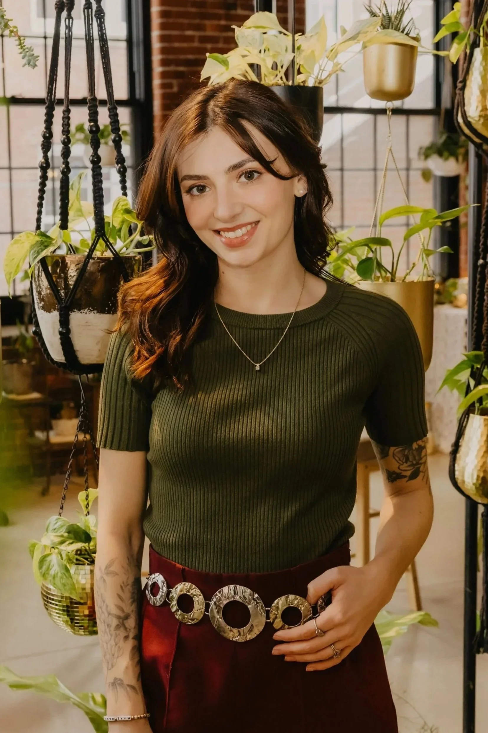A young woman with wavy hair lying on a fur rug, looking at a tarot card book and tarot cards, with a colorful paisley jacket and dark pants in a cozy, vintage-style room with velvet furniture and a candle.