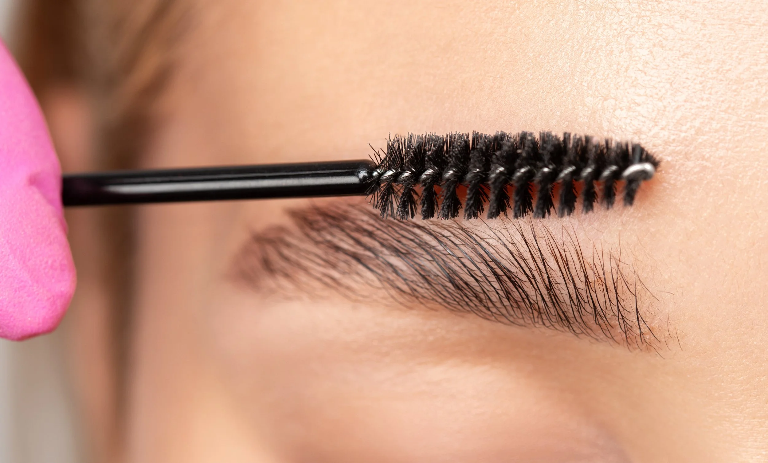 A close-up image of a person's eyebrow with a brush going through the hairs, showing off the high quality of brow shaping services done at Flirt Custom Lash Studio Toronto. 