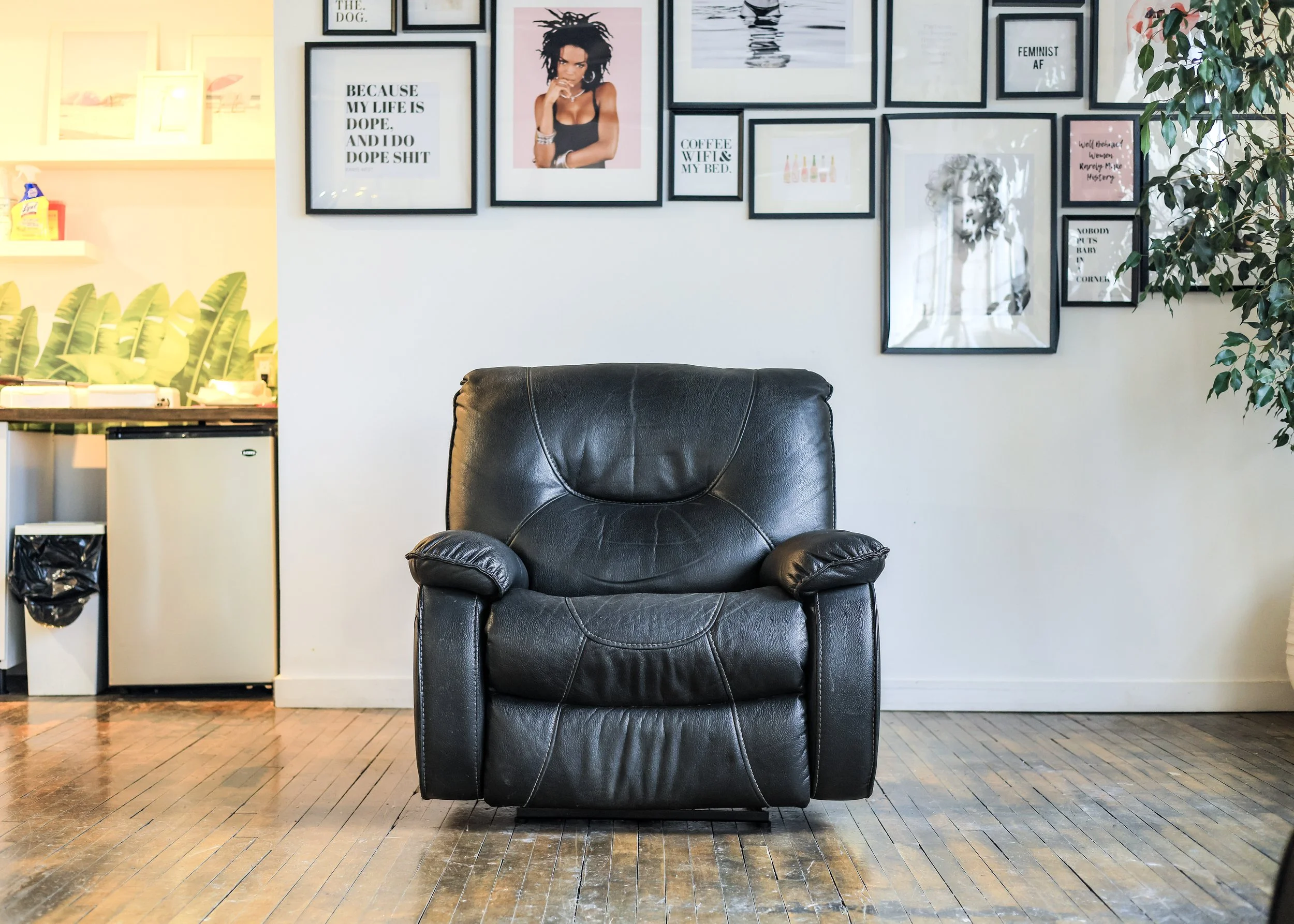 A black leather recliner sits in front of a wall of framed prints, creating a cozy treatment spot. The setup showcases the relaxing atmosphere at Flirt Custom Lash Studio for eyelash extensions and brow lamination.