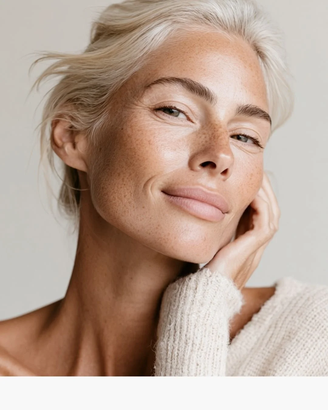 An image of a woman smiling with her cheek resting on her hand, with glowing skin and a defined jawline, showcasing the results of a Gua Sha facial at Flirt Custom Lash Studio Toronto.