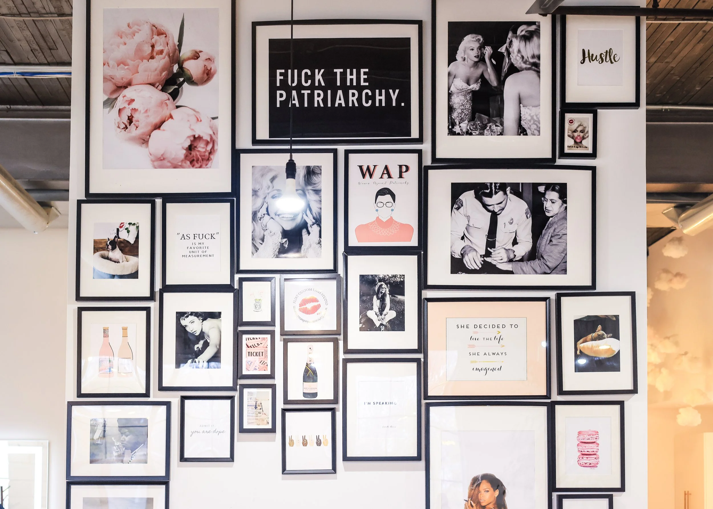 A gallery wall of framed art and bold quotes decorates the studio, creating an empowering backdrop. It reflects the style and vibe of Flirt Custom Lash Studio offering eyelash extensions and brow lamination.