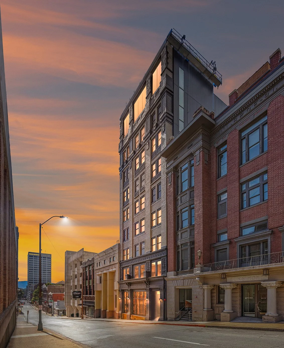 City street during sunset with multi-story buildings, some with lit windows, and a streetlamp on the left.