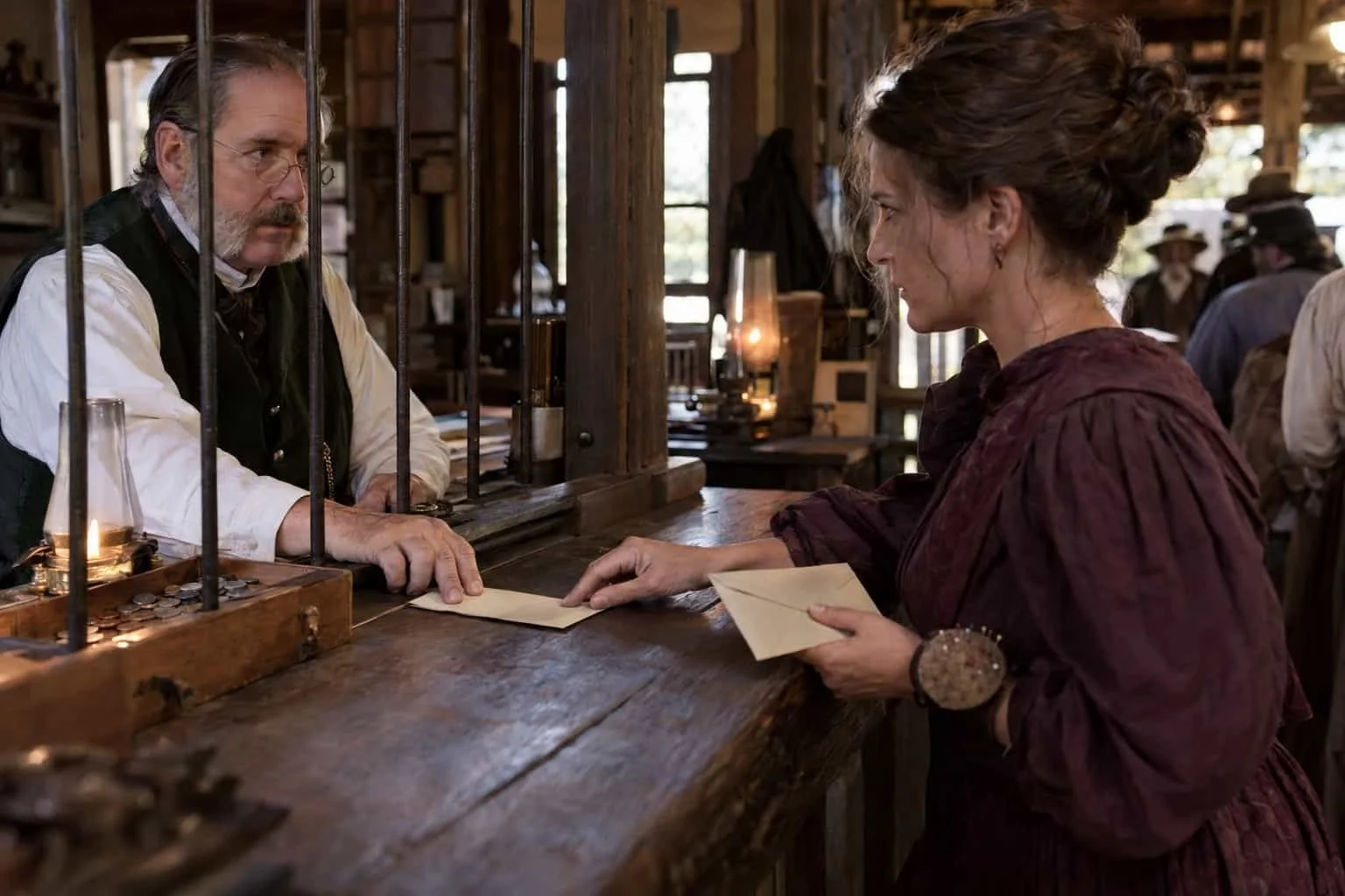 In an 1890s payday recreation, a paymaster gives a seamstress two envelopes, keeping a finger on the rent one.
