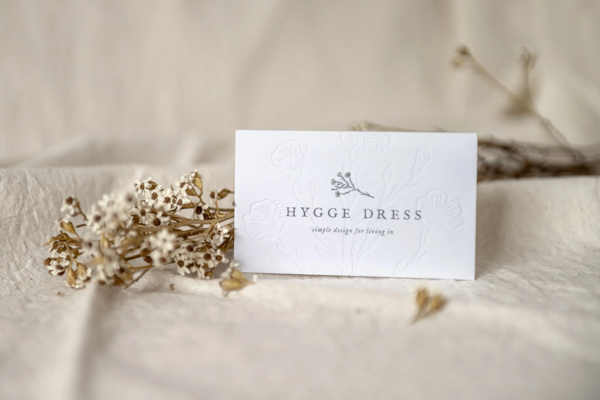 White business card with a blind emboss that reads 'Hygge Dress'.