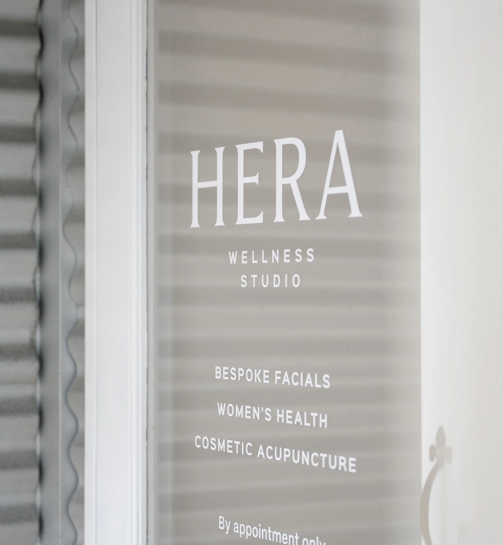Close-up of a glass door with a white signage decal using the Hera Wellness Studio branding.