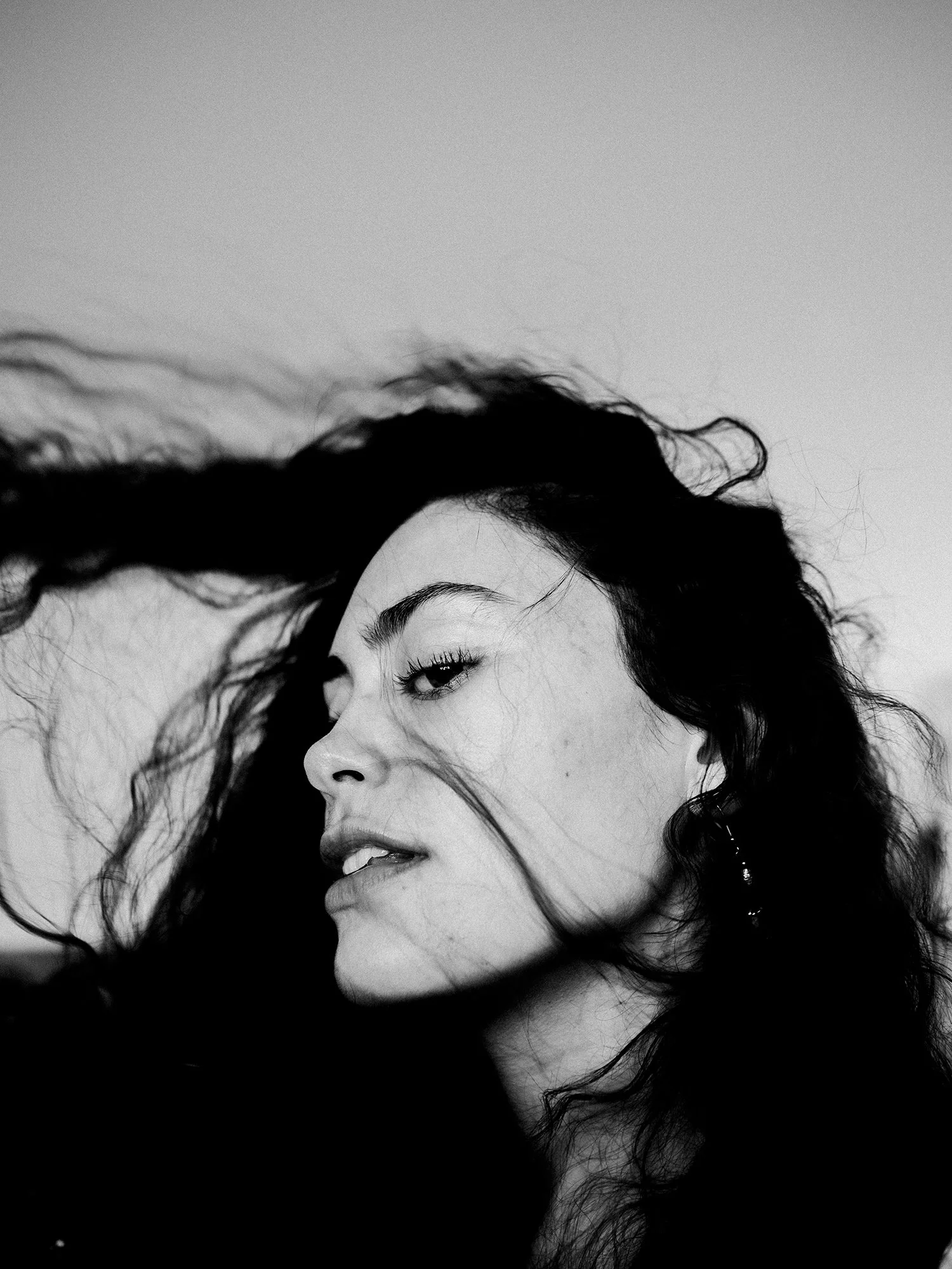 Black and white close-up photo of a woman with long hair blowing across her face, with a serene expression and her eyes slightly closed.