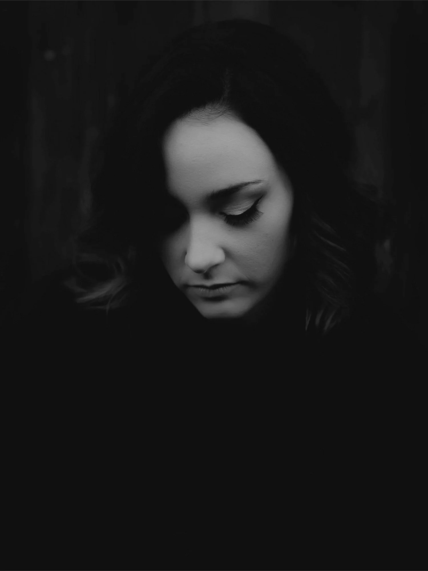 A close up portrait of a woman with dark hair looking down