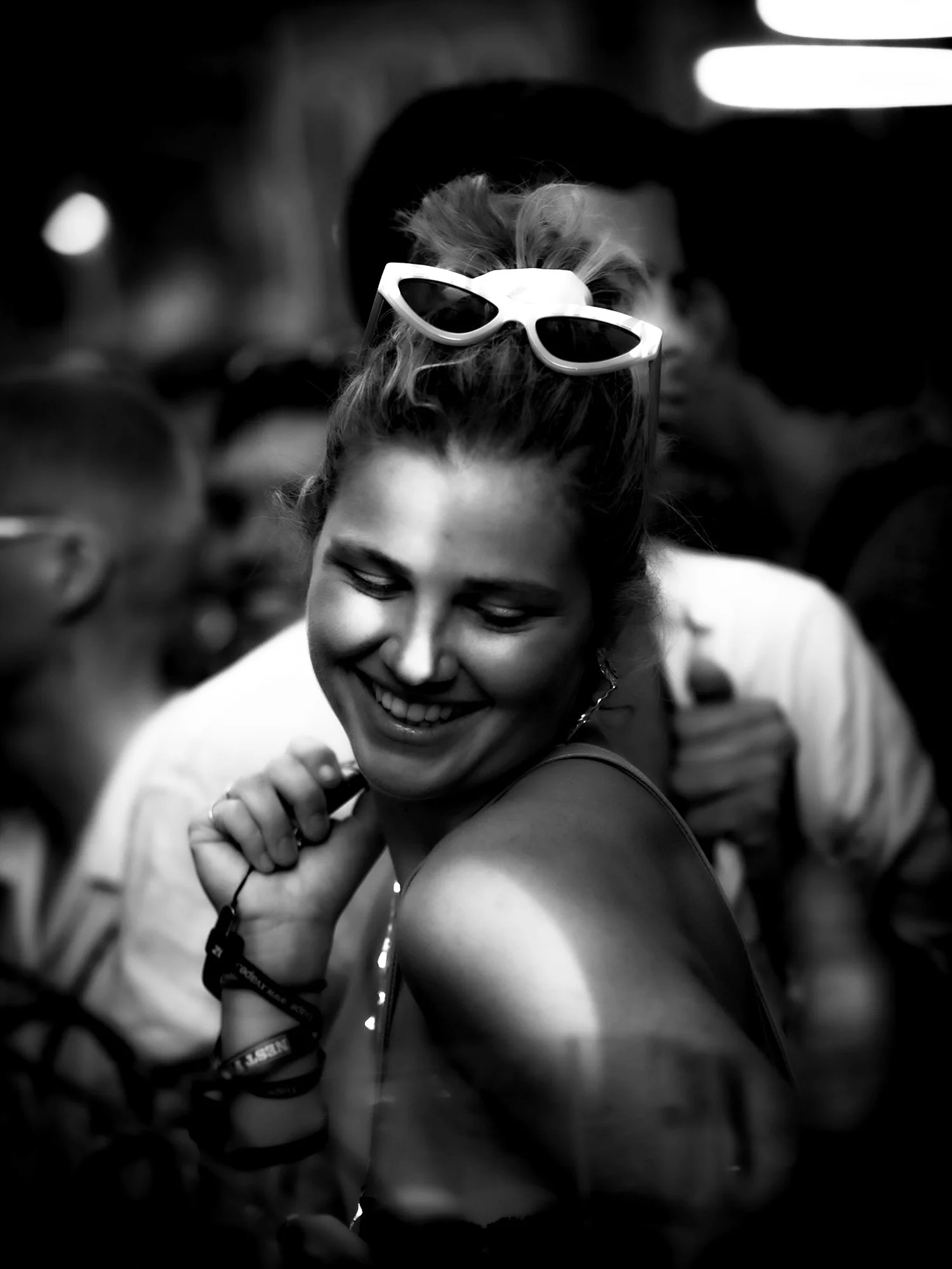 Smiling woman with sunglasses on her head dancing at a crowded party in black and white.