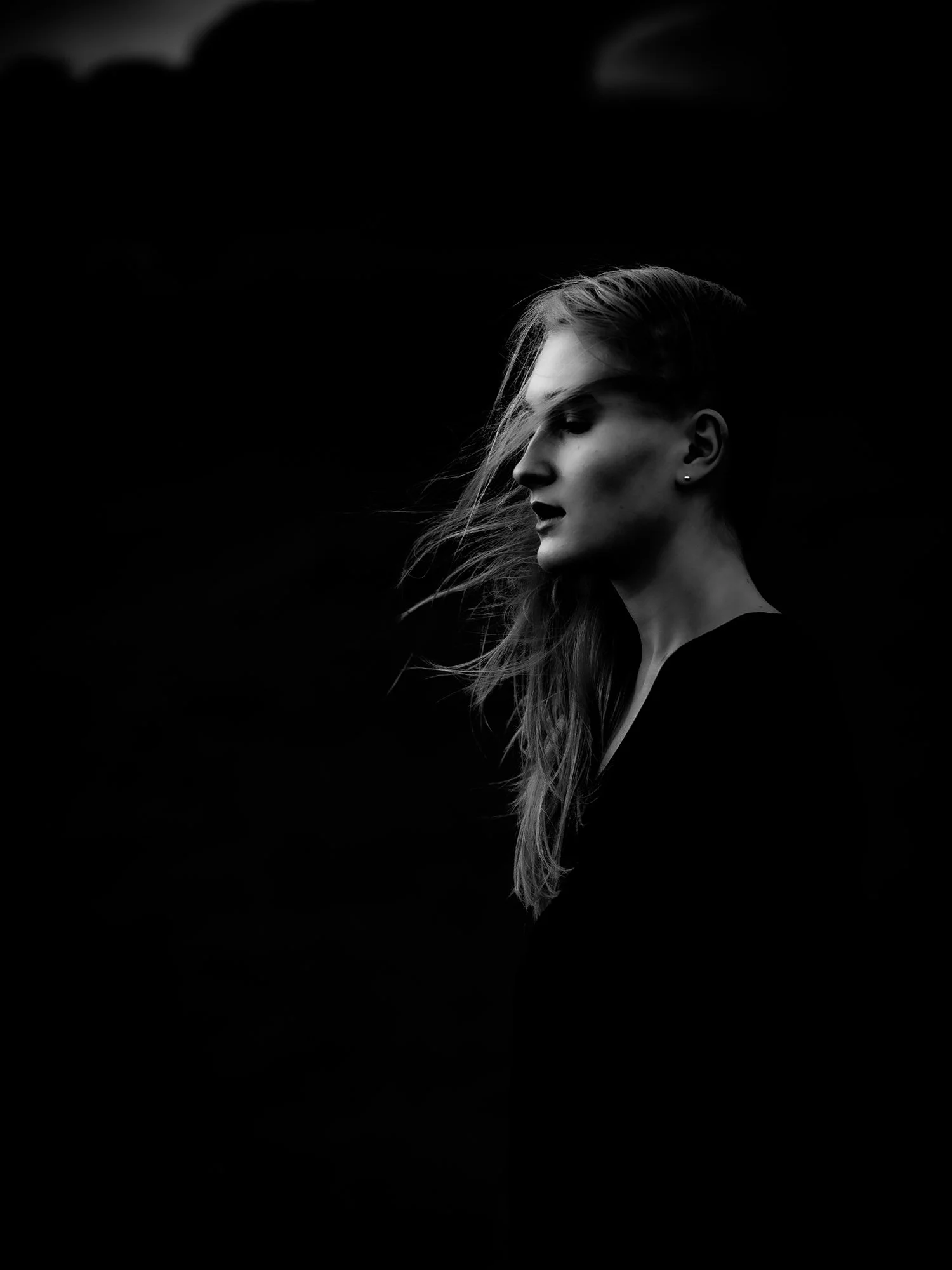 Black and white side profile of a woman with long hair, looking down, against a dark background.