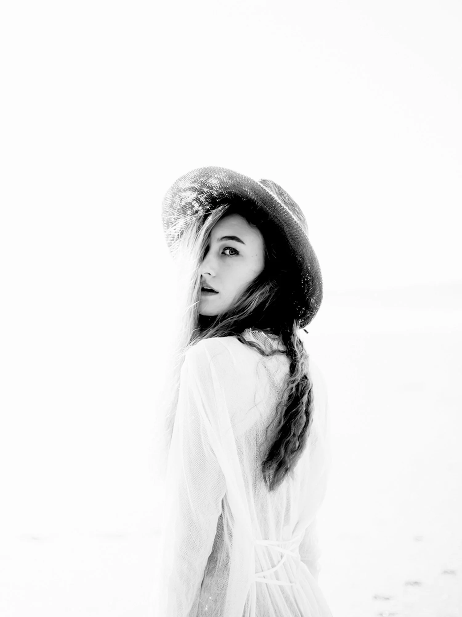A woman with long hair twisting to the side and wearing a hat stares back to the camera