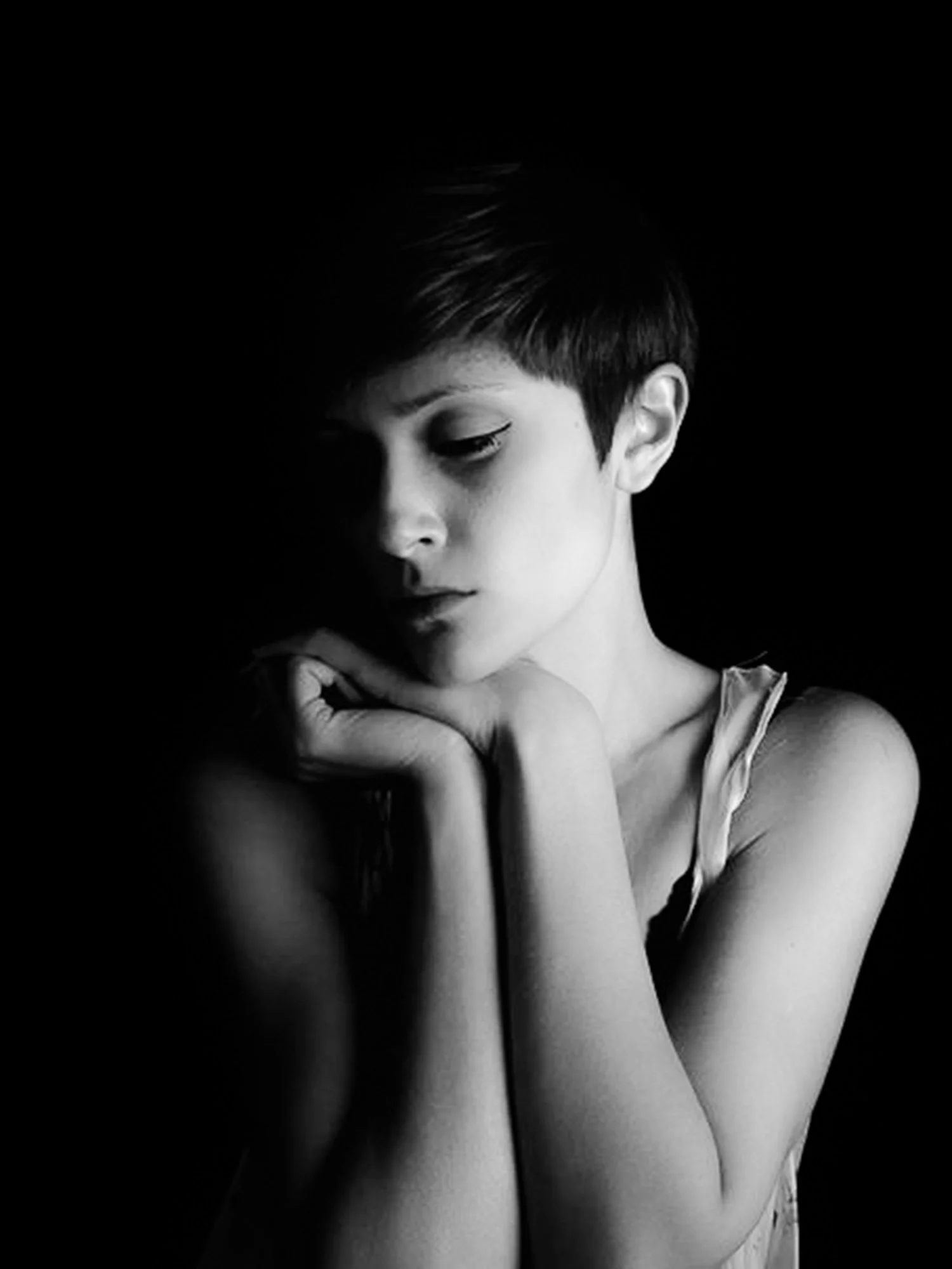 A woman in a dark room with light on her face rests her chin on her hands