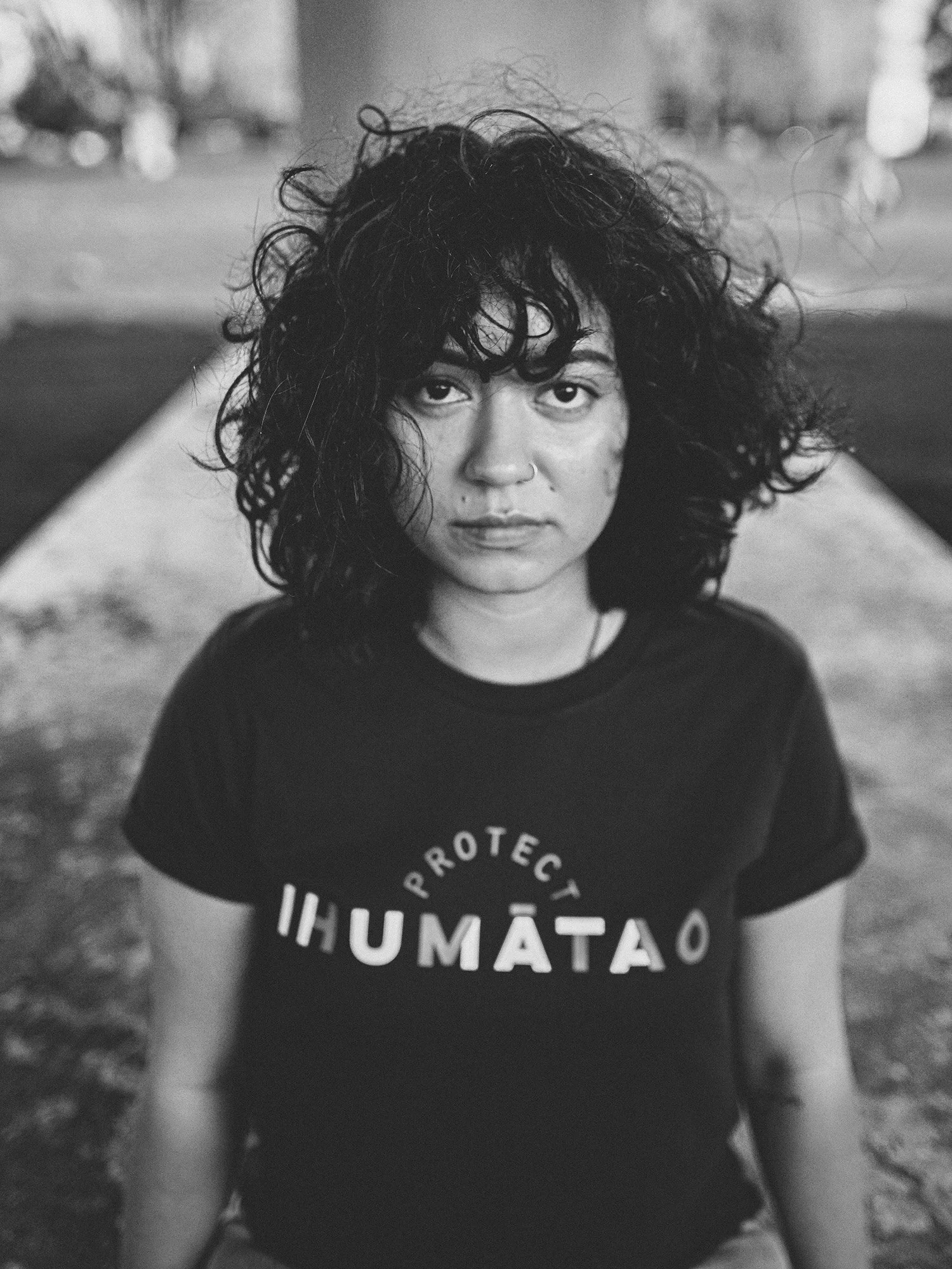 A woman with dark hair and wearing a t shirt sits under a bridge