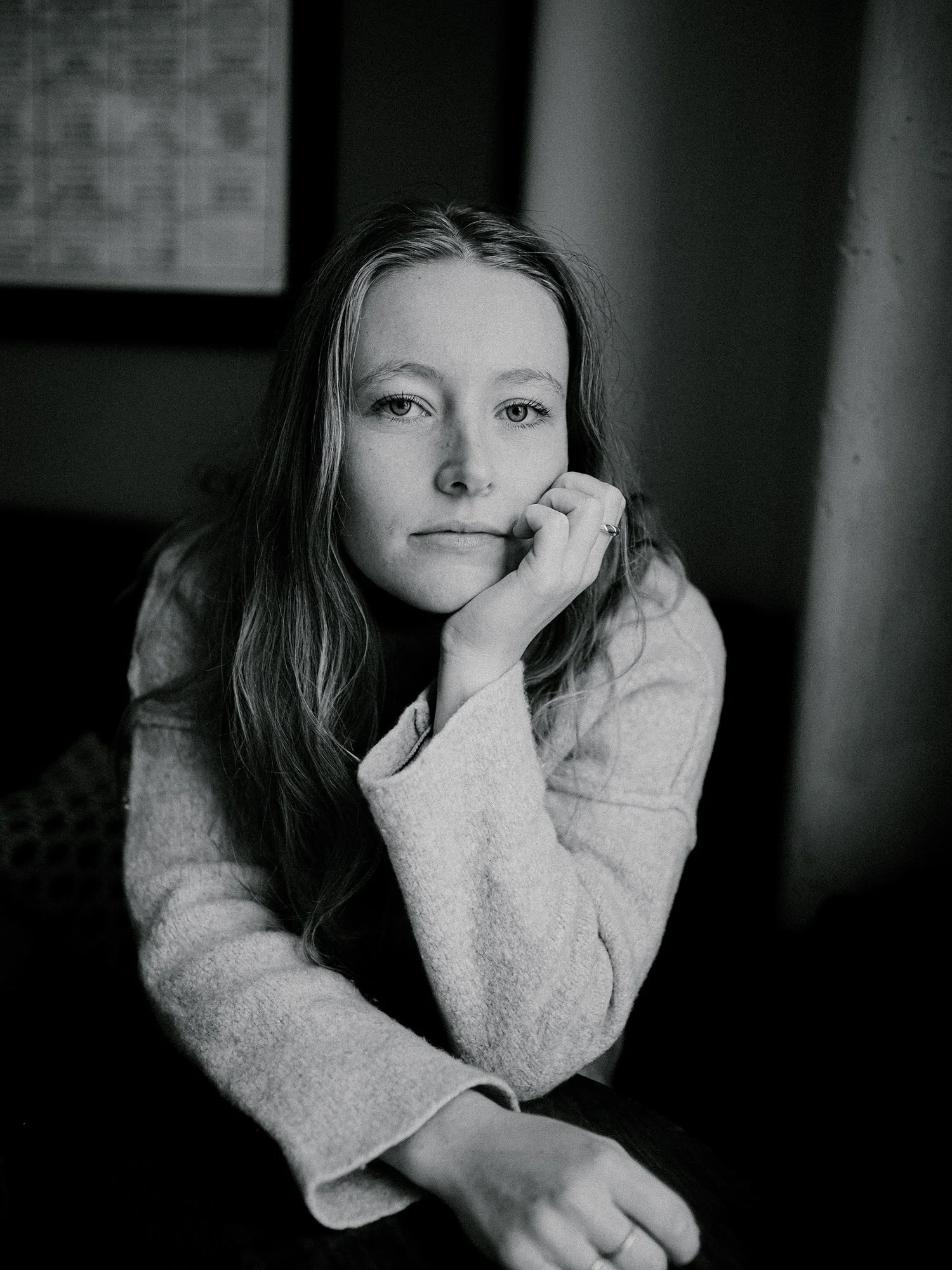 A black and white portrait of a young woman with long hair, resting her chin on her hand, looking at the camera with a thoughtful expression.
