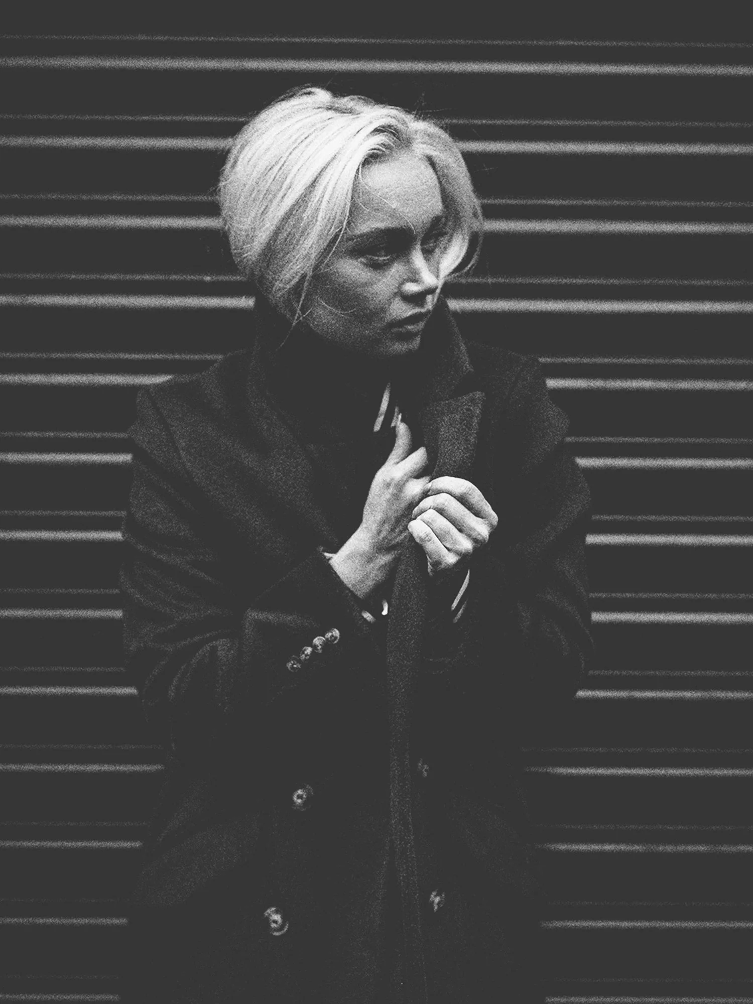 A woman with blonde hair looks to the side as she stands in a street