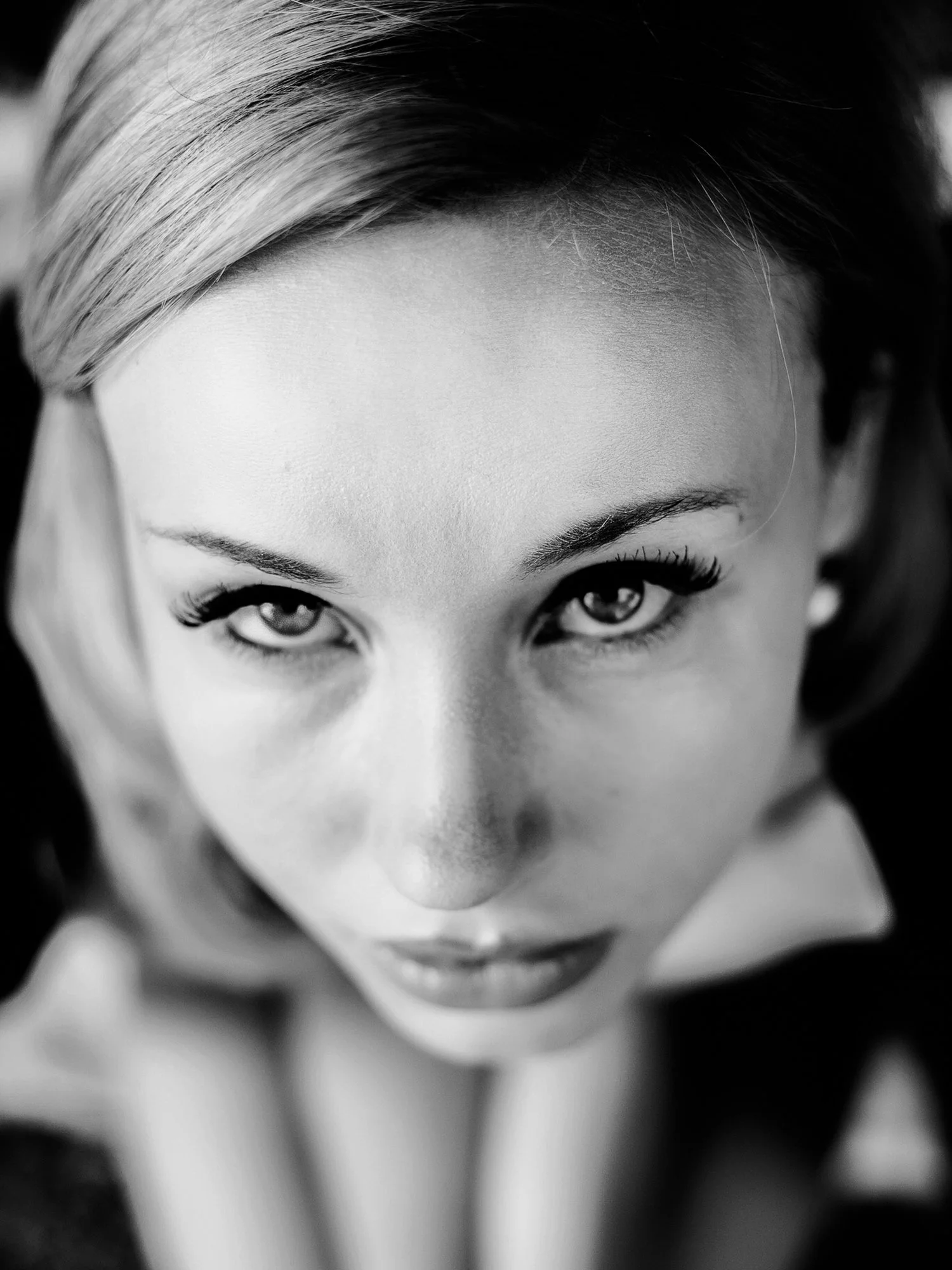Close-up black and white photo of a woman's face taken from above, with intense gaze and well-defined features.