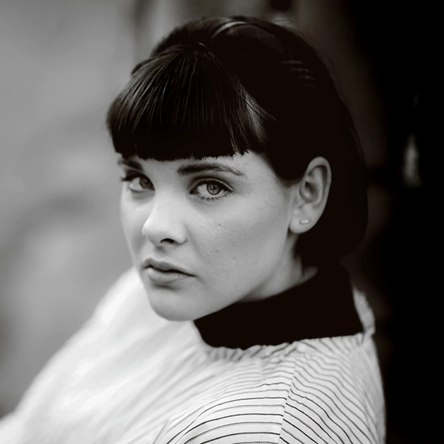 Black and white portrait of a woman with short dark hair and light eyes, wearing a striped top.