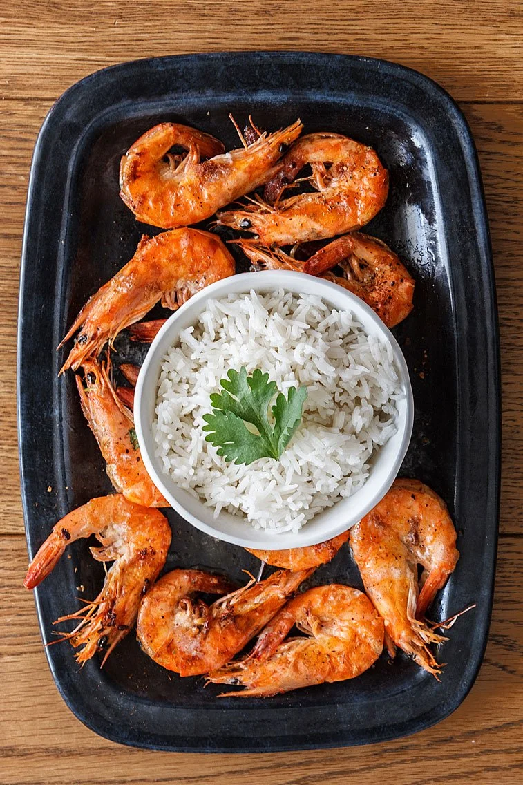 Cooked shrimp with a serving of white rice garnished with a cilantro leaf
