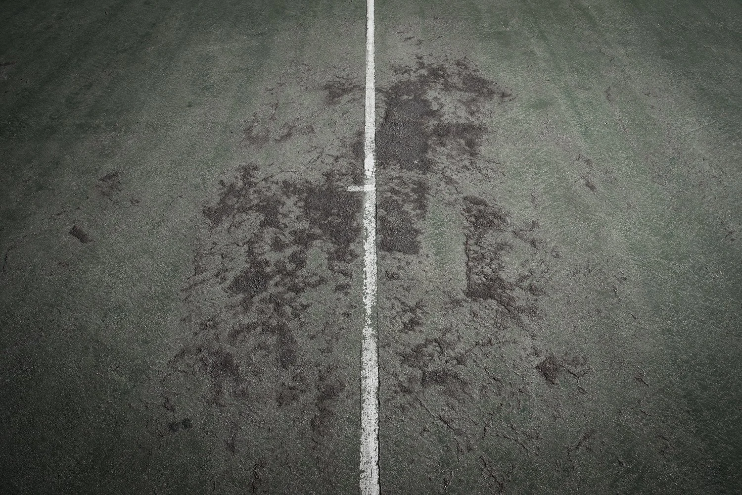 Top-down view of a worn basketball court surface with a white line dividing the court in the center.