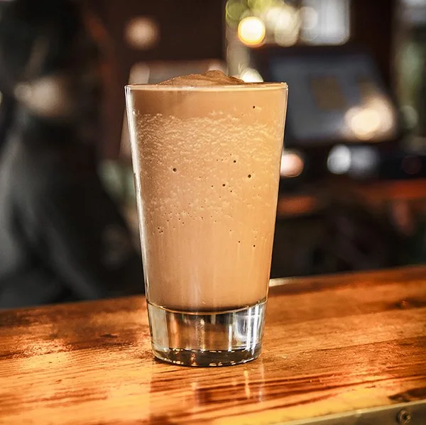 A glass of iced coffee or latte on a wooden surface in a dimly lit environment.