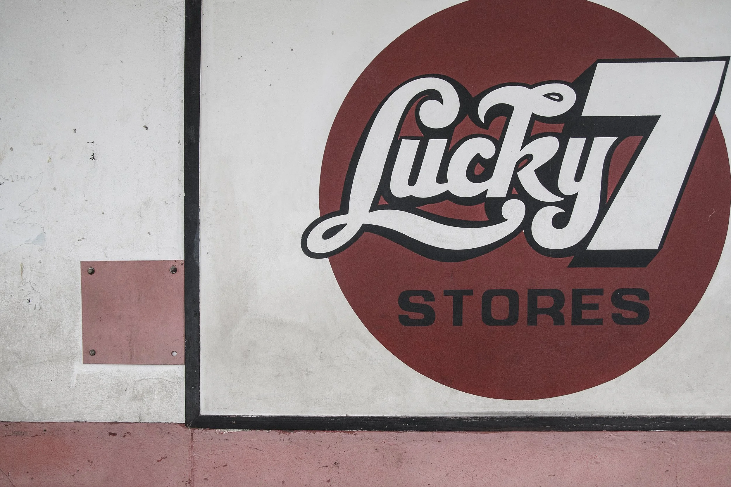 Sign on a wall with a red circle and black text that says 'Lucky 7 Stores'