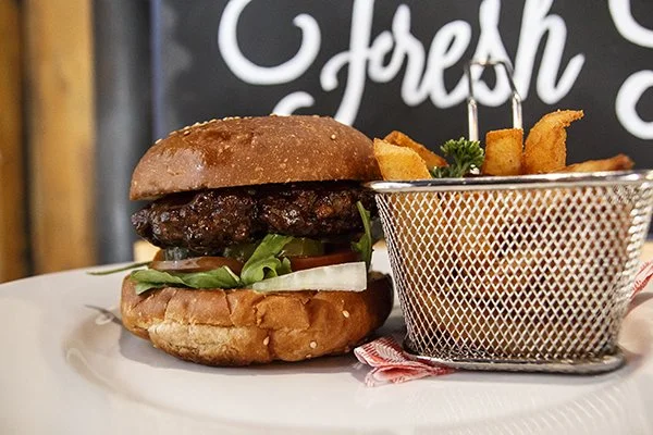 Burger with lettuce, onion, tomato, and beef patty in a bun, served with a side of French fries in a metal basket.