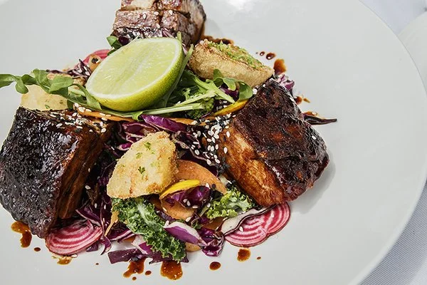 Grilled fish with dark, crispy skin served on a bed of colorful pickled vegetables and greens, garnished with lime and crispy bread crumbs.