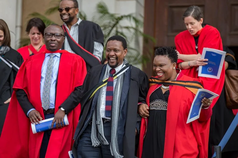 Group of graduates in academic cap and gown, celebrating and smiling at a graduation ceremony.
