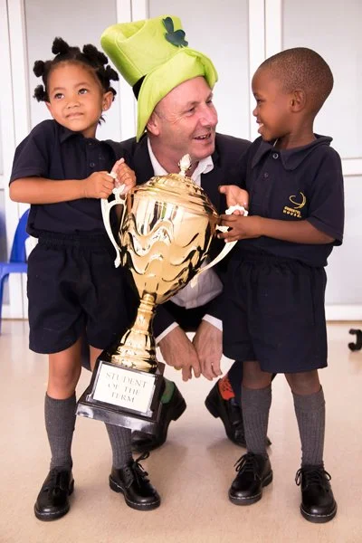 Two children and an adult with a gold trophy at school
