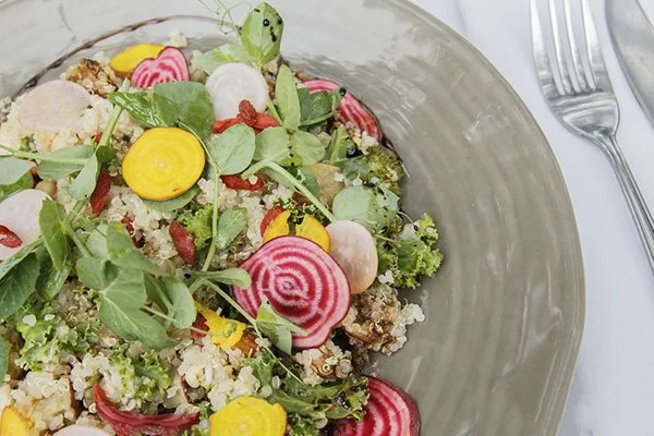 Close-up of a colorful salad with radish slices, yellow carrot slices, leafy greens, and chopped vegetables in a gray bowl.