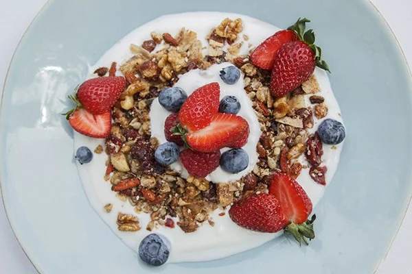Granola with strawberries and blueberries served over yogurt on a light blue plate.