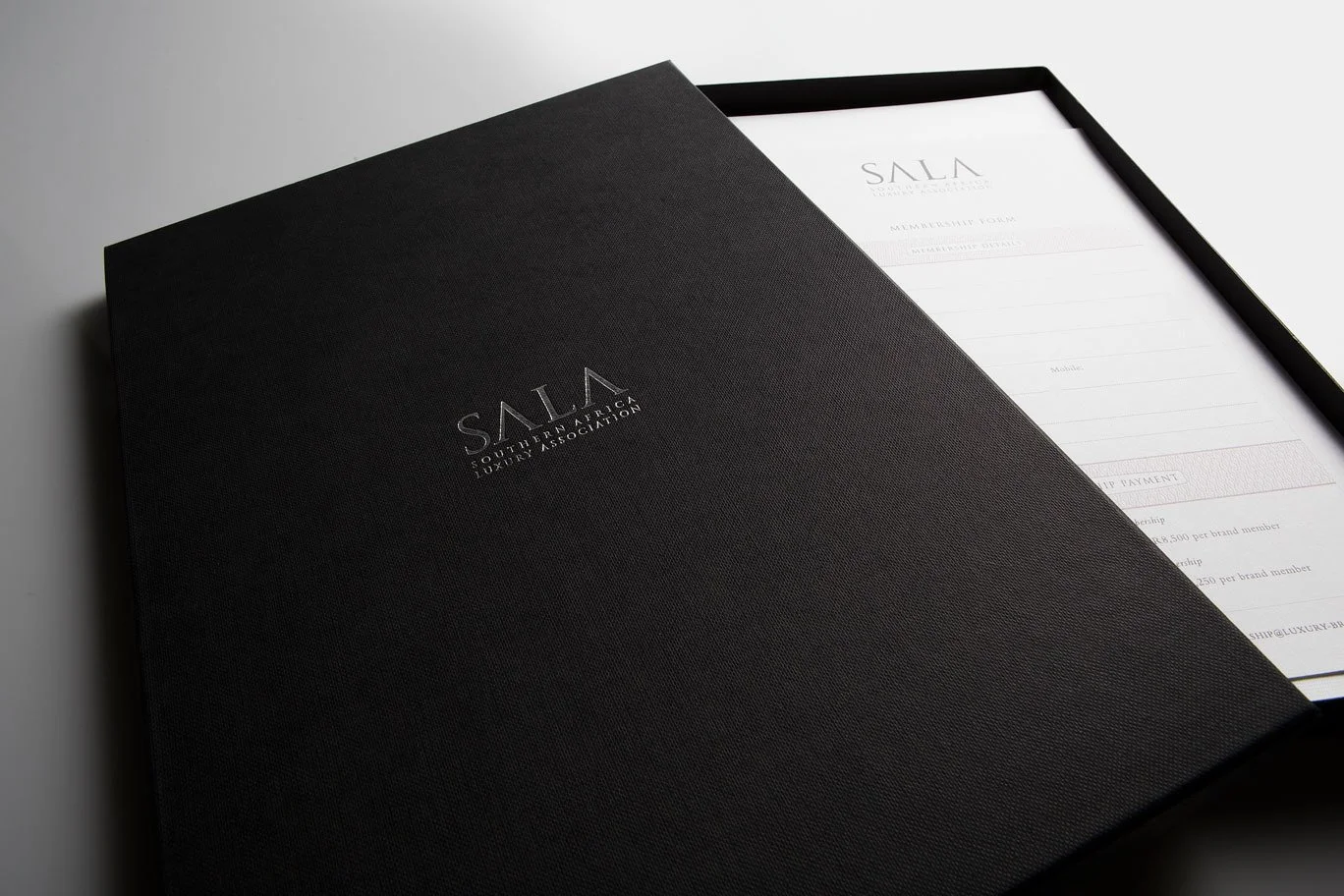 Black folder with silver logo reading 'South Atlantic Luxury Association' partially open to reveal a document inside.