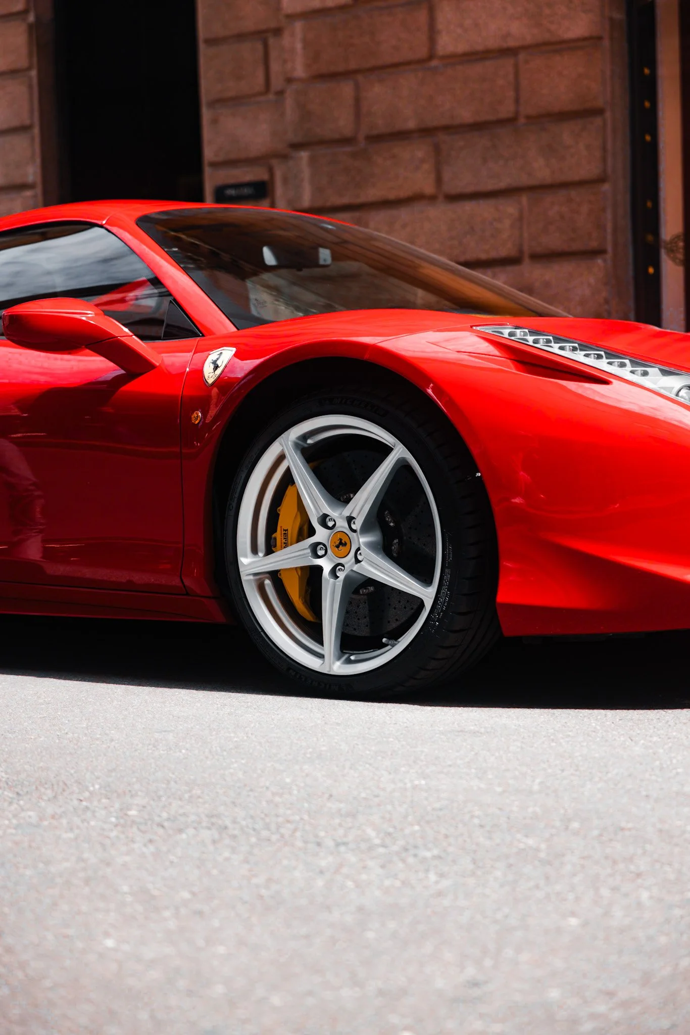 Close-up of a red Ferrari sports car parked on the street in front of a brick building.