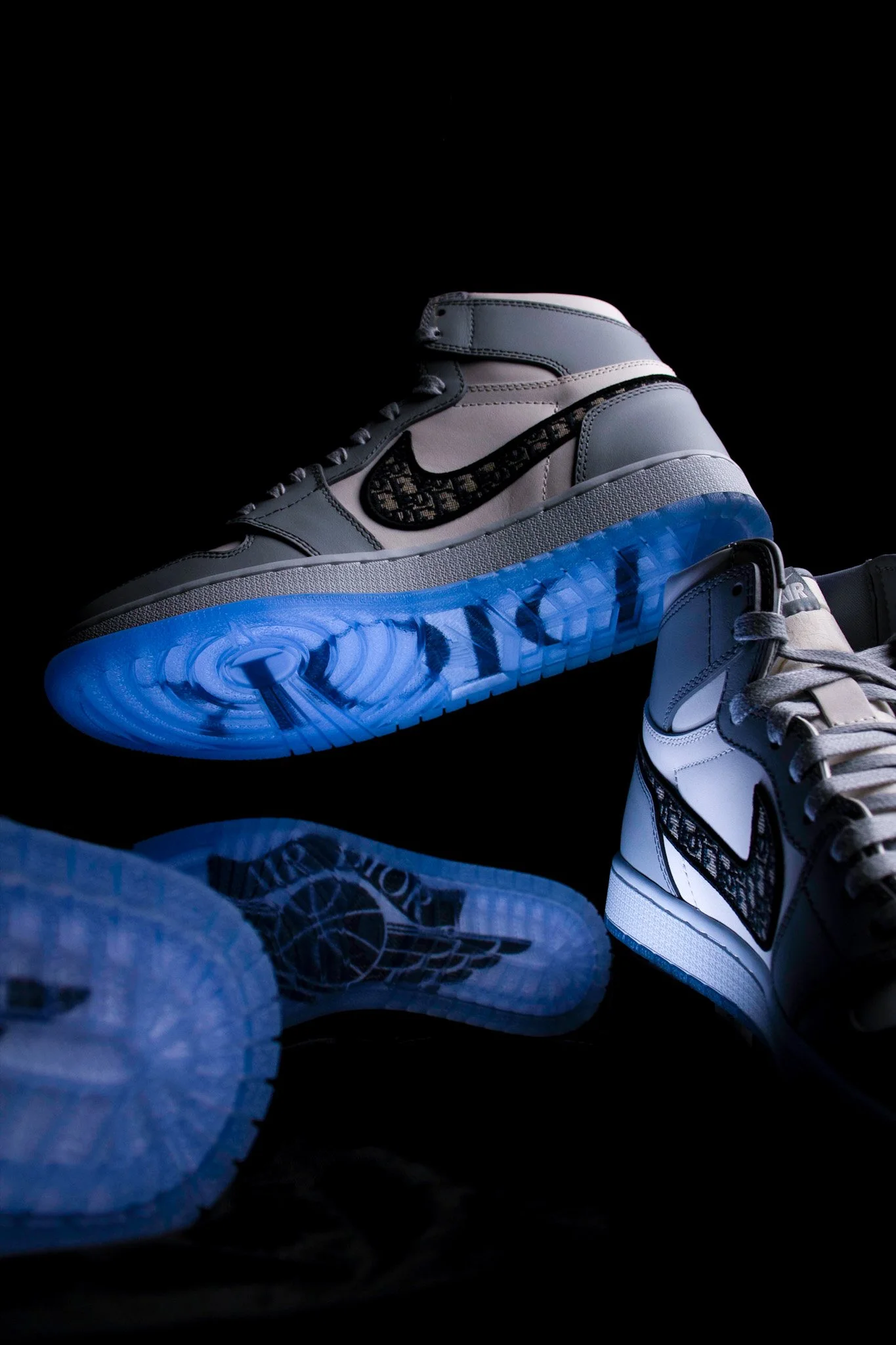 Close-up of a pair of Nike sneakers with a black and brown pattern on the swoosh logo and a blue sole, styled with other sneakers and denim pants, set against a dark background.