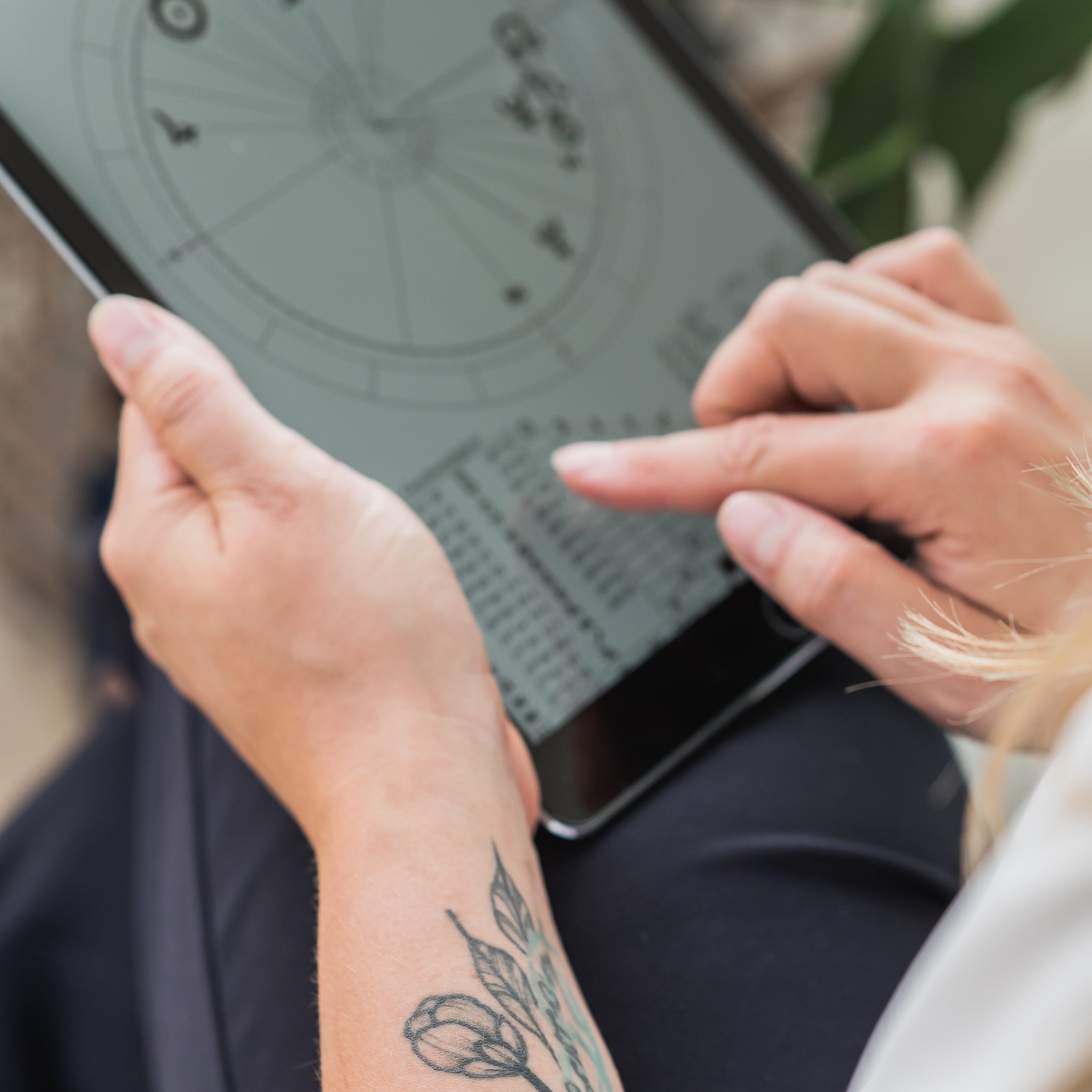 Person mit Tablet betrachtet Horoskop-Diagramm, Nahaufnahme der Hände mit Tätowierung.