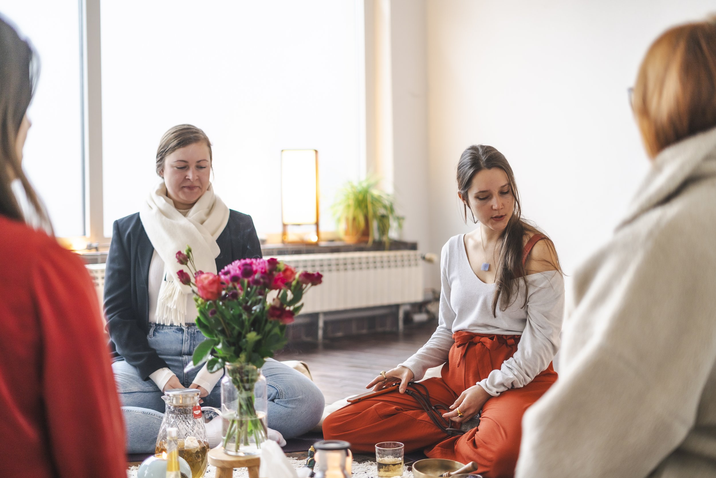 Eine Gruppe von Frauen sitzt in einem Raum auf dem Boden, umgeben von Blumen und Teelichtern, bei einem Frauenkreis.