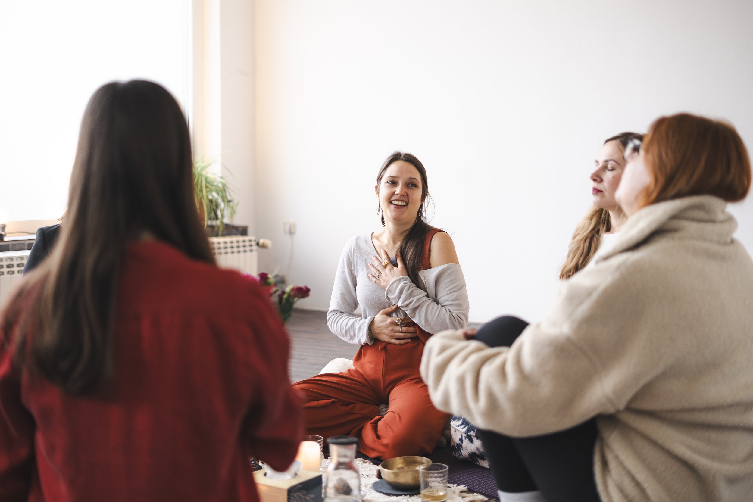 Vier Frauen sind in einem Frauenzirkel, llächeln und scheinen in ein Gespräch vertieft zu sein. Kerzen und eine Klangschale sind in der Mitte platziert, was auf eine meditative oder entspannende Aktivität hinweisen könnte.
