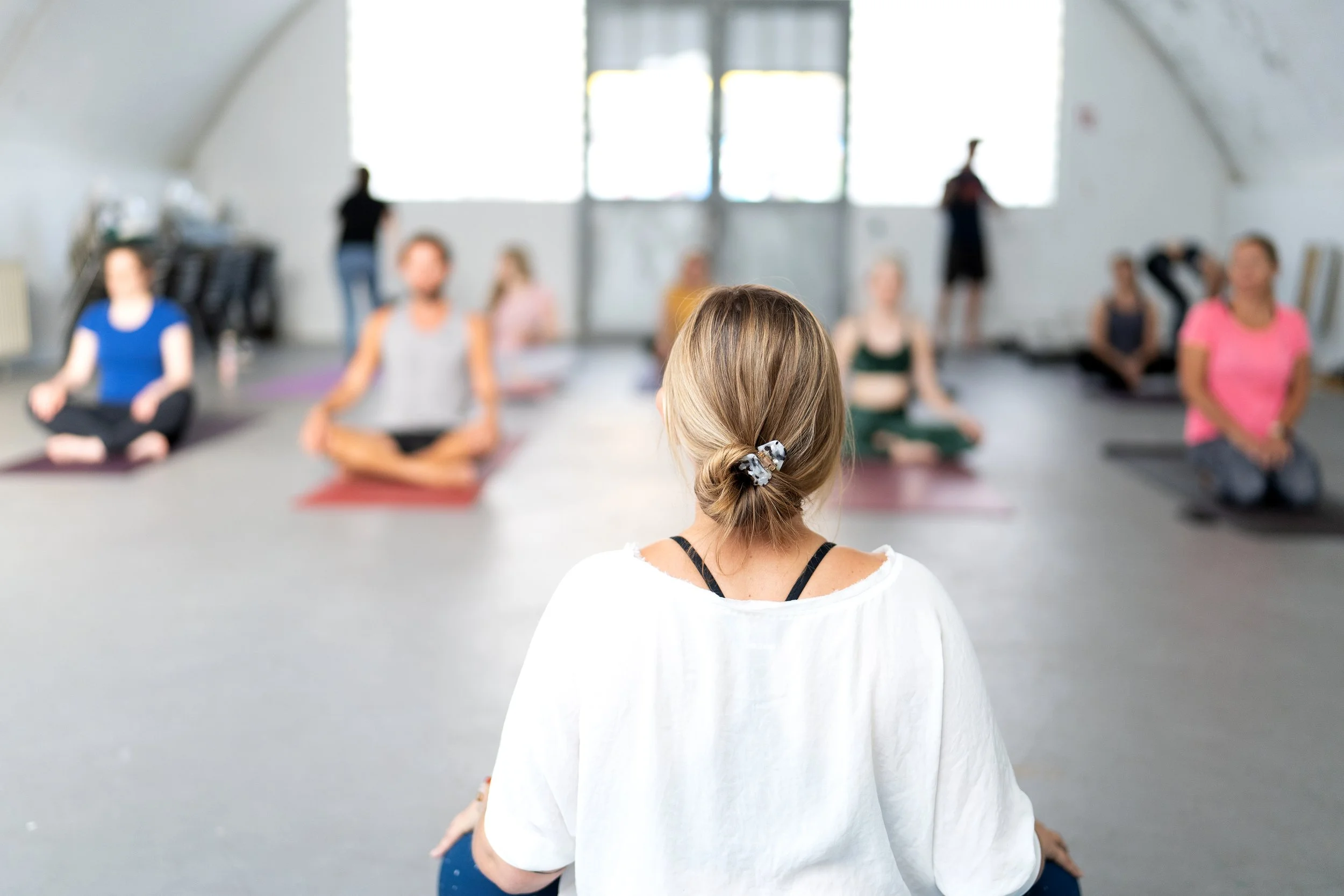 Eine Gruppe von Menschen sitzt auf Yogamatten in einem Raum und macht eine Meditation oder Yogapraxis.