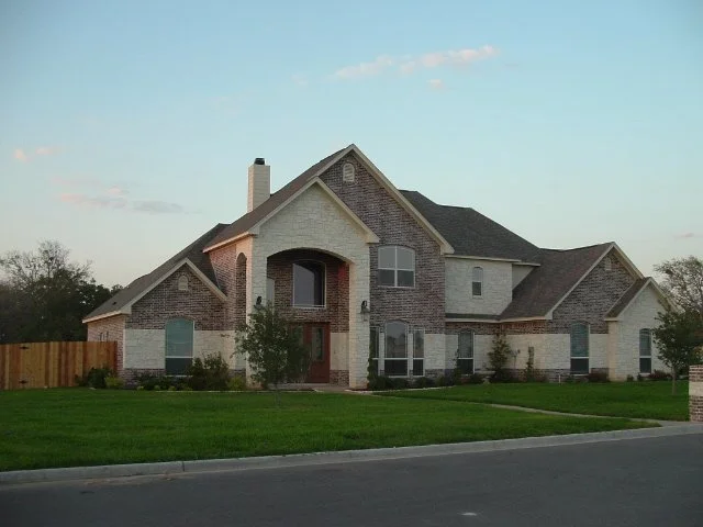 A large two-story house with brick and stone exterior, multiple gabled roofs, a front porch, and well-maintained lawn.