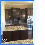 Kitchen with dark wood cabinets, granite countertop island, and stainless steel appliances.