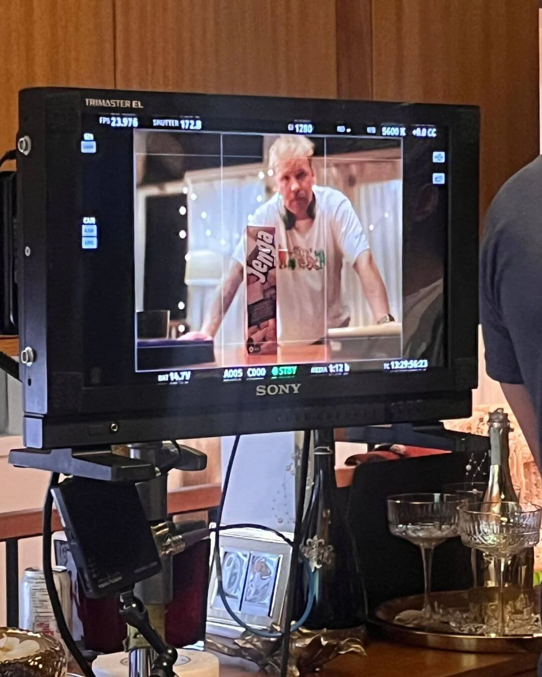 A camera monitor showing a man with white hair and a white t-shirt, standing behind a table with a box of Jenga.
