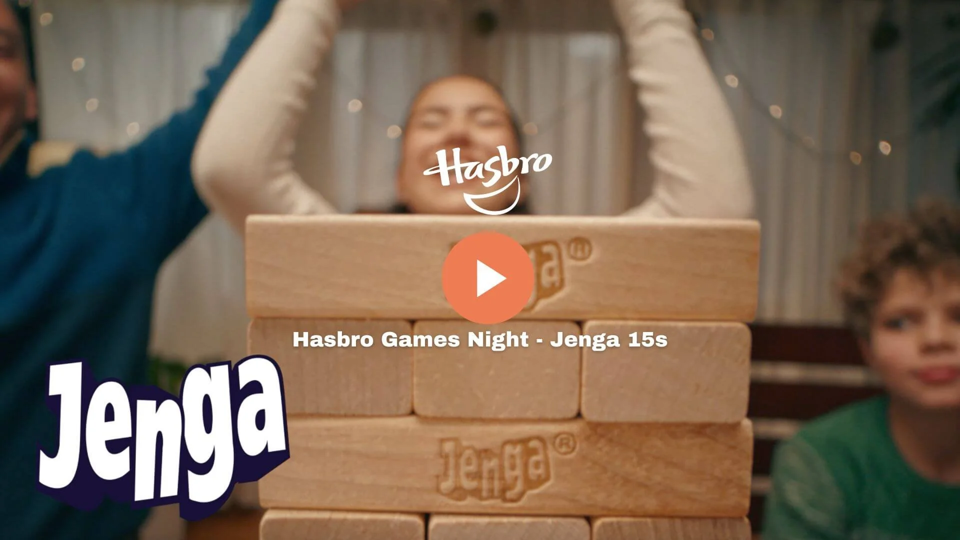 Two children playing Jenga during a Hasbro Games Night, with a stacked wooden Jenga tower in the foreground and two children smiling and watching in the background.
