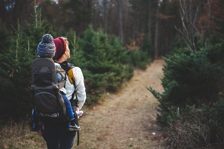 Two women hiking through a forest with a trail, carrying backpacks and dressed warmly in winter hats and jackets.