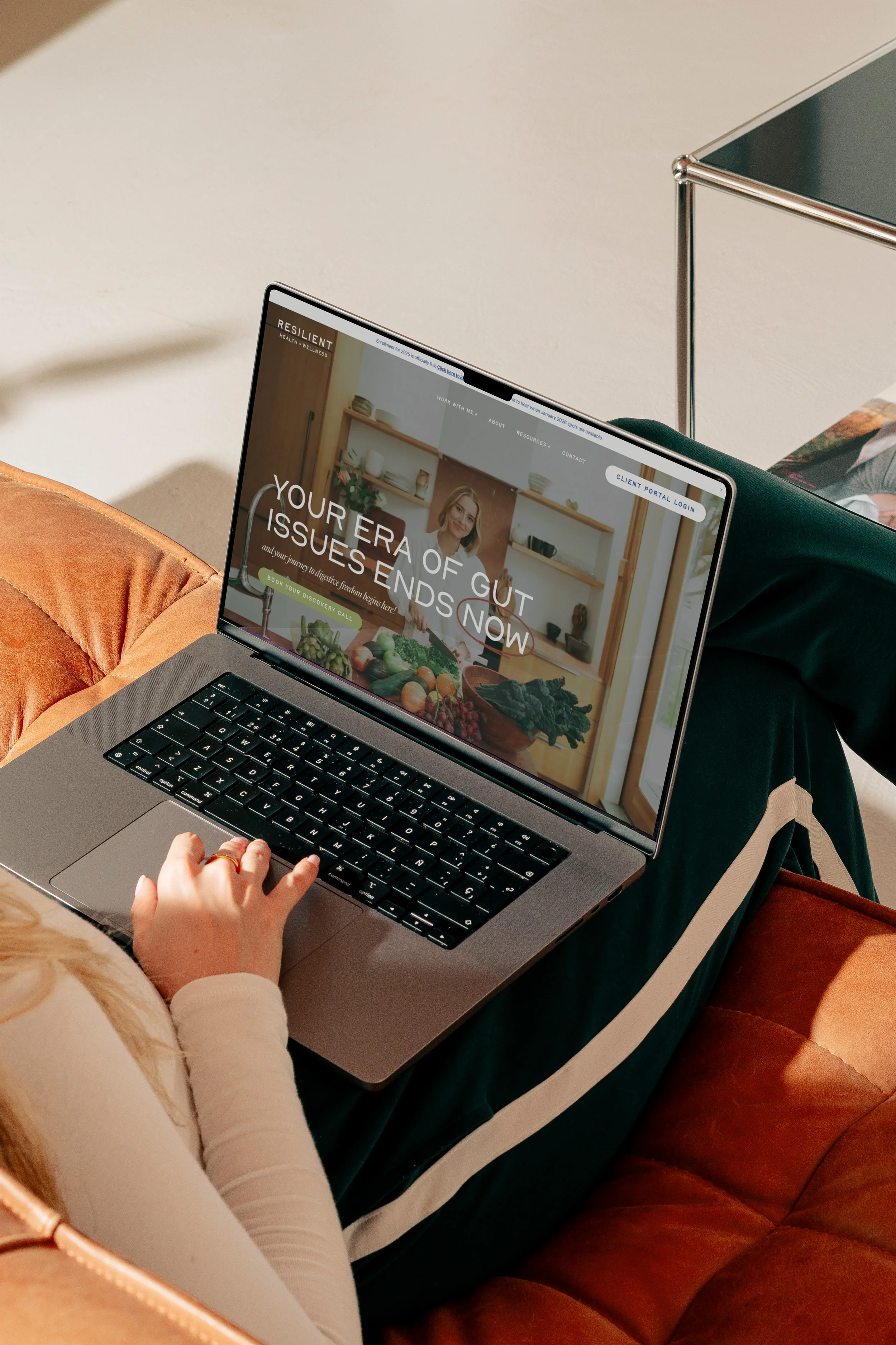 Laptop on a person's lap displaying a website about gut health and issues, with a woman in the background in a kitchen.