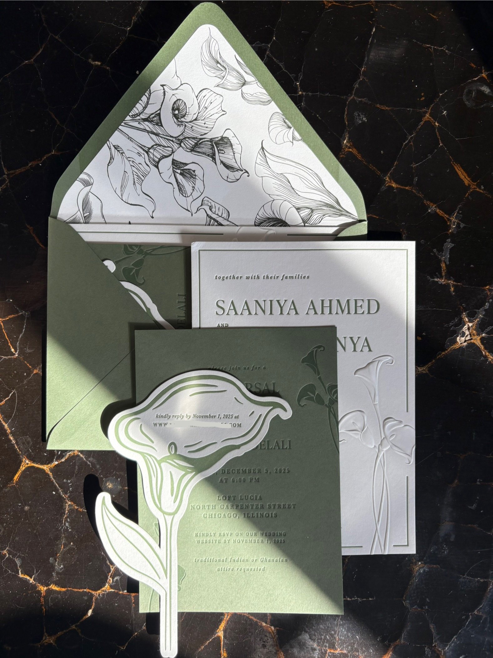 A set of elegant wedding invitations and RSVP card on a dark marble surface, featuring floral and calla lily motifs with a green and white color scheme.