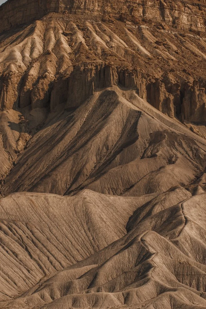 Eroded desert landscape with layered, brownish rock formations and steep ridges.