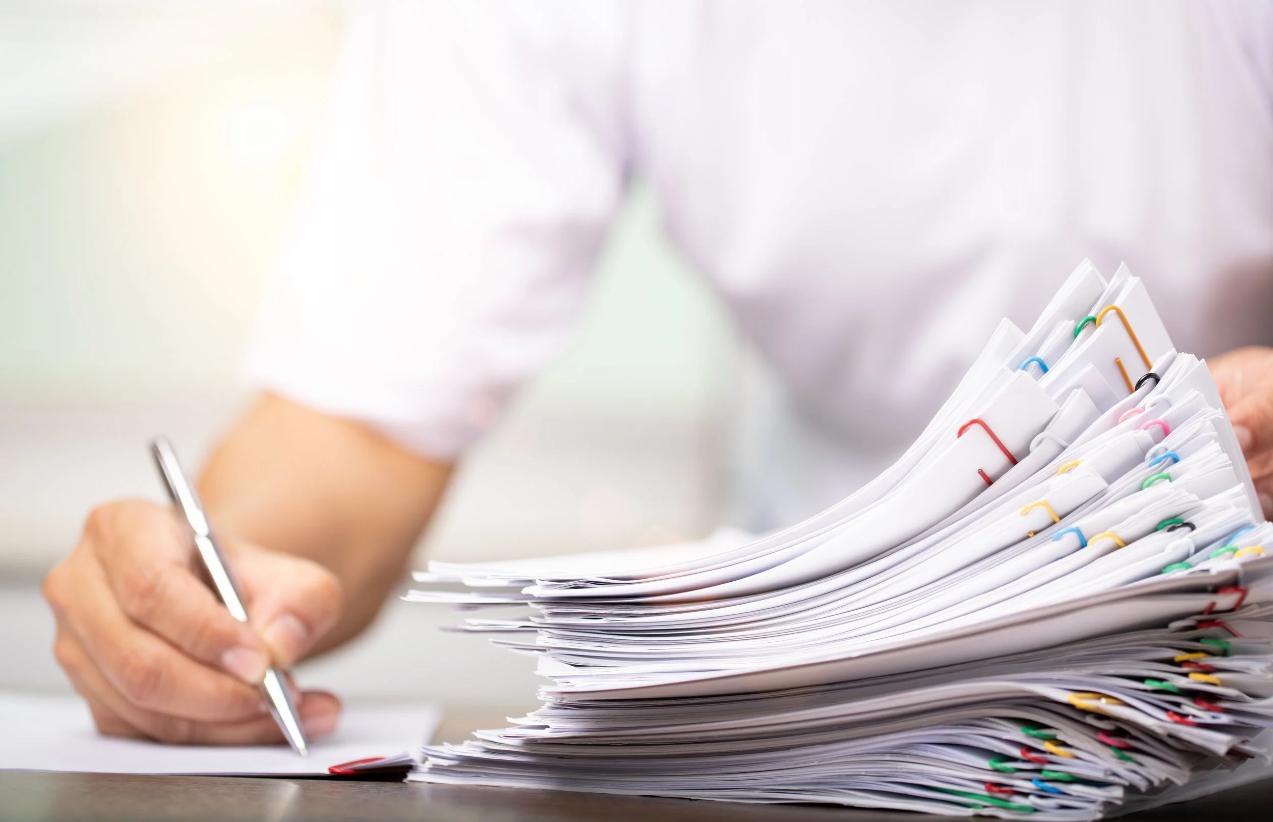 Close-up of a person holding a pen and organizing a large stack of papers with colorful paperclips.